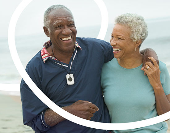 Man wearing Mobile PERS walking on beach with wife
